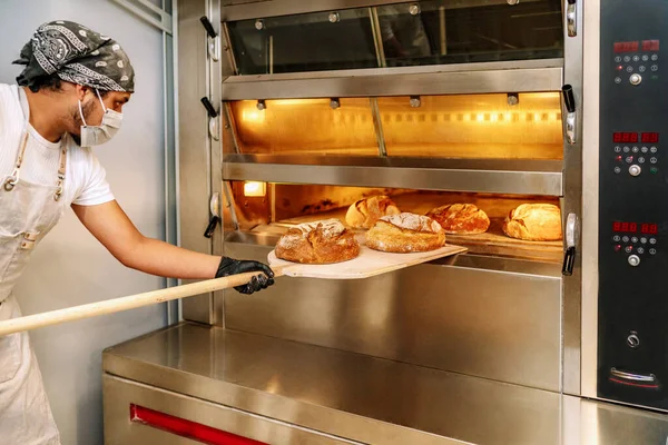 Latin fırıncının 2020 Covid19 Coronavirus salgınından dolayı fırına eldiven ve maskeyle ekmek koyduğu seçici odak noktası