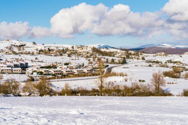 Çok mavi gökyüzü ve beyaz bulutları olan karlı bir köy görebileceğiniz güzel bir manzara ve uzaktaki dağları görebilirsiniz.