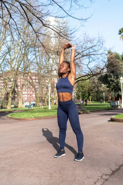 Siyah kadın ısınıyor ve fiziksel antrenmana başlamak için kaslarını esnetiyor ya da halka açık bir parkta koşuyor.