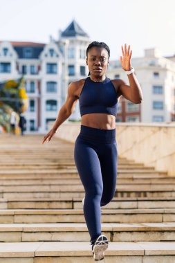 Kaçak gibi giyinmiş siyah afro kız gün batımında şehirde merdivenlerden aşağı koşuyor.