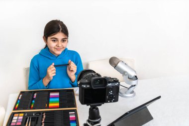 Genç nüfuzlu ve blogcu oturma odasından canlı yayın yapan pastel boya sınıfına gülüyor ve kameraya bakıp bir video veya sosyal medya platformunda mikrofona konuşarak harika vakit geçiriyor.