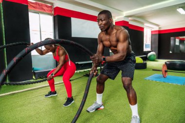Spor salonunda iki siyah vücut geliştirme sporcusu kollarını ve göğsünü güçlendirmek için çok çaba sarf ederek aerobik halat egzersizi yapıyorlar. Bedenini spor salonunda güçlendirme kavramı