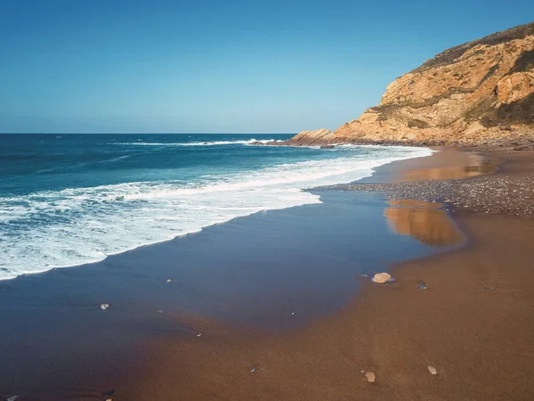 Kayalık ve kumlu sahilde bir sürü dalgası olan uçurumların insansız hava görüntüsü.