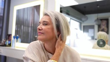 Güzel, olgun bir kadın yeni saç stiliyle mutlu ve kendinden emin hissediyor. Kuaförde saçlarını yavaş çekimde sallıyor.