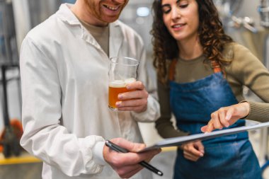 Bira fabrikasındaki işçiler bira örneği alıyor ve kalite kontrolü yapıyor. Üretim sürecinde yüksek standartları sağlıyorlar.