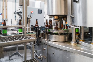 Kahverengi cam şişeler taşıyıcı bant boyunca hareket ediyor. Fabrikanın bira üretim süreci boyunca doldurup kapatıyorlar.