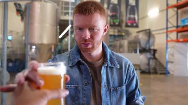 Kızıl saçlı yakışıklı bir bira bardağını tadıyor. Rengini, içkisini inceler ve bir bira fabrikasında kameraya gülümser.