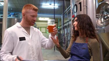 Erkek ve dişi bira üreticileri taze bira rengini, aromasını ve tadını inceliyor. İki gülen işçi ürün kalitesinden bahsediyor.