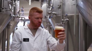 Beyaz önlüklü profesyonel bira ustası modern bir bira fabrikasında yeni dökülmüş bira rengini, berraklığını ve köpüğünü kontrol ediyor.