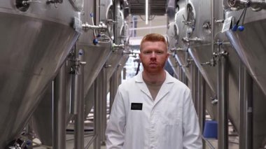Beyaz laboratuvar önlüğü giyen, bira fabrikasında çelik fermantasyon tanklarının arasında duran, kızıl saçlı yakışıklı bir bira ustası.