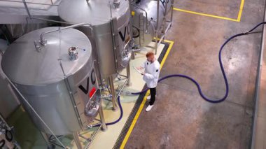 Bira yapımcısının demleme sürecini yüksek açılı izlemesi. Uzman makineleri kontrol ederken panoya yazı yazıyor.