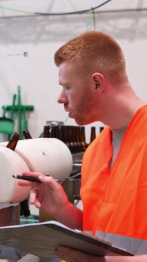 Genç erkek fabrika çalışanı otomatik taşıma sistemi üzerinde kalite kontrolü yapıyor. İşçi bira fabrikasında cam şişeleri kontrol ediyor.