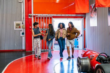 Bir grup sırıtkan arkadaş go kart pisti tesisinde birlikte yürüyor, eğlence ve eğlencenin tadını çıkarıyorlar.