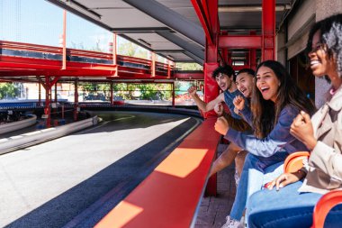 Çeşitli arkadaşlar, heyecan verici go kart yarışlarını izliyor, seyircilerin tezahüratları açık bir pistte duruyor, eğlence ve eğlencenin tadını çıkarıyor.