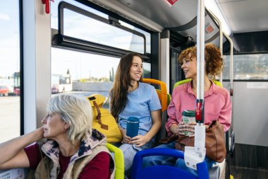 Genç bayan arkadaşlar şehir otobüsünde konuşmaktan zevk alıyorlar, birlikte seyahat ediyorlar ve toplu taşıma araçlarını kullanıyorlar.