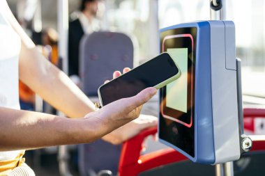Modern seyahat ve teknolojiyi temsil eden, şehir otobüsündeki ulaşılamayan bir okuyucuya cep telefonu ödemesi yapan bir kadın.