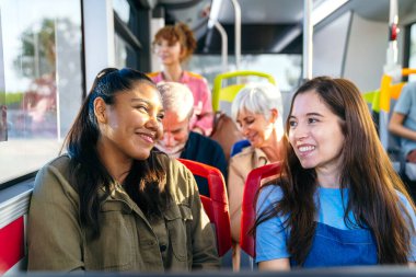 Diğer yolcularla birlikte bir halk otobüsünde seyahat ederken gülümseyen ve konuşan genç kadınlar. Kentsel seyahat ve arkadaşlık konsepti