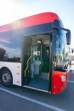 Açık bir ön kapısı ve kırmızı ve beyaz renkleri olan şehir otobüsü, pencerelere yansıyan çevre, toplu taşımaya hazır