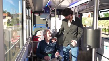 Toplu taşımada seyahat eden engelli yaşlı bir yolcuya yardım ve yataklık teklif eden şefkatli genç bir adam.