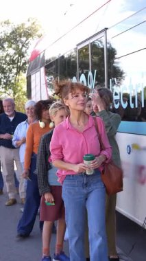 Bir otobüs durağında sırada bekleyen bir grup insan. Pembe gömlekli kadın işe gidip geldiği için toplu taşıma aracına biniyor.