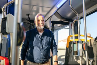 Şehir otobüsünde giderken gülümseyen kıdemli adam, şehir seyahatini ve ulaşılabilir ulaşımı temsil ediyor.