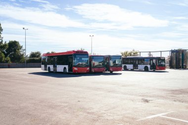 Modern kırmızı ve beyaz şehir otobüs filosu temiz gökyüzünün altındaki depoda günlük toplu taşıma ve banliyö hizmeti için hazır bekliyor.
