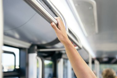 Bir kamu otobüsünün içindeki destek kolunu tutan banliyö çalışanı, şehir ulaşımını, güvenliği ve günlük yolculuğu temsil ediyor.