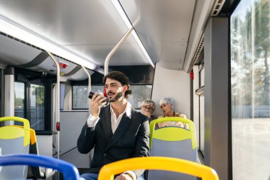 Umumi bir otobüste akıllı telefonuyla konuşan genç bir adam işe giderken ses asistanı kullanıyor.