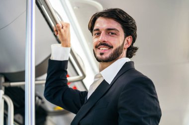 Resmi kıyafetli gülümseyen adam, şehir otobüsünde seyahat ederken tutunacak bir şey tutuyor ve günlük seyahat kavramını sunuyor.