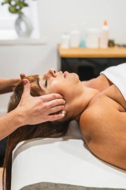 Kadın uzanmış, temporomandibular ekleminde fizyoterapi masajı yaptırıyor, TMJ bozukluğunu tedavi ediyor, rahatlık ve sağIık buluyor.