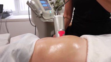 Profesyonel terapist, bir kadının beline başları dönen modern bir aletle derin bir fizyoaktif masaj yapıyor.