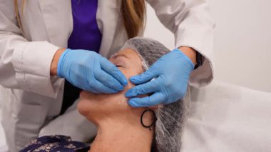 Kozmetik uzmanı, olgun bir kadına yaşlanma karşıtı bir yüz prosedürü uyguluyor. Doktor cilt gerdirme ve gençleştirme için doldurucu enjekte ediyor.