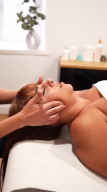 Rahatlamış bir kadın bir fizyoterapistten tedavi edici bir çene ve yüz masajı alıyor. Temporoçene eklem ağrısı için profesyonel tedavi