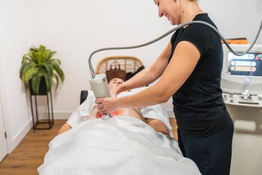 Terapist bir kadının midesine başlık takıyor. Sağlık ve güzellik için derin bir fizyoaktif masaj yapıyor.