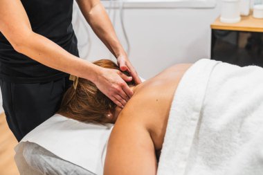 Sağlık uzmanı spa yatağında yatan birine boyun ve omuz masajı yaparak rahatlamayı ve stres atmayı teşvik ediyor.