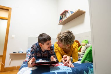 Yatakta yatıp dijital tablet kullanırken birbirlerine bakan, Down sendromlu anne ve çocuğu sevmek