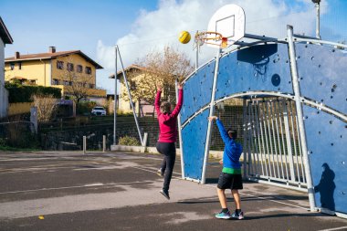 Gençlikten ve aktif yaşam tarzından zevk alan iki sağlıklı çocuk mavi gökyüzünün altında bir halk sahasında spor yapıyorlar.