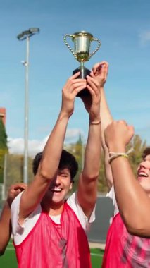 Bir grup heyecanlı genç futbolcu şampiyonluk zaferini kutluyor. Mutlu takım ağır çekimde altın kupayı kaldırıyor.