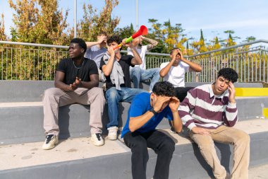 Diverse group of young male football fans showing disappointment and sadness while watching a game in stadium stands