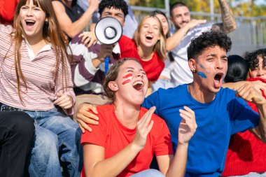 Çeşitli coşkulu hayranlar spor müsabakalarını kutluyor. Stadyum tribünlerinde insanlar heyecan ve destek gösteriyor.