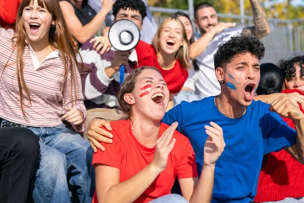 Çeşitli coşkulu hayranlar spor müsabakalarını kutluyor. Stadyum tribünlerinde insanlar heyecan ve destek gösteriyor.