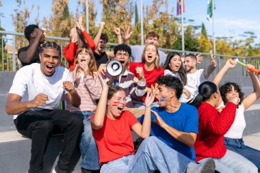 Çok ırklı gençler tribünlerden takımlarını aktif olarak destekliyor, heyecan ve coşku ifade ediyorlar.