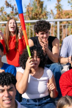 Genç hayranlar stadyumda spor müsabakalarını izleyip tezahürat yapıyorlar. Bir grup arkadaş oyun için heyecanlanıyor