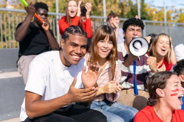 Stadyumdaki bir spor müsabakasını izleyen bir grup coşkulu genç arkadaş heyecanla bağırıp alkışlıyorlar.