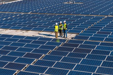 Kask ve yelek mühendisleri, yenilenebilir enerji ve sürdürülebilir gücü tartışan geniş bir çatı güneş paneli dizisini inceliyor.