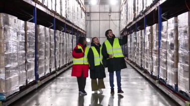Farklı meslektaşlardan oluşan bir ekip bir dondurucu deposundan geçiyor. Elinde barkod tarayıcısı olan bir yönetici envanter kontrol sistemini açıklıyor.