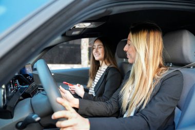 İki profesyonel kadın araba kullanıyor, gülümsüyor ve tartışıyorlar. İş ya da iş seyahatleri için aynı aracı kullanıyorlar.