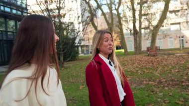 Sonbaharda bir şehir parkında güzel bir yürüyüş yapan iki gülen arkadaş. Sarışın bir kadın ve esmer bir kadın konuşup gülüyor.