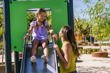Anne ve kızı parkta bir oyun parkında birlikte eğleniyorlar, çocukluk aktiviteleri sırasında gülüyorlar ve iletişim kuruyorlar.