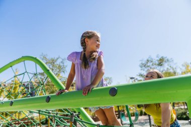 Anne ve kızı boş zamanların tadını çıkarıyorlar, canlı yeşil bir tırmanma ağıyla şehir parkında oyun oynuyorlar.